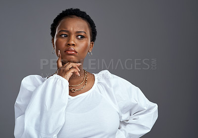 Buy stock photo Shot of a young woman looking thoughtful while posing against a grey background