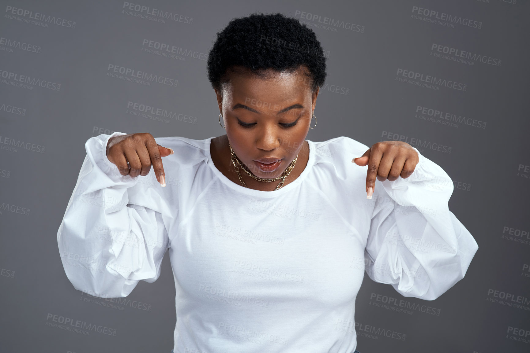 Buy stock photo Shot of a young woman pointing down while standing against a grey background