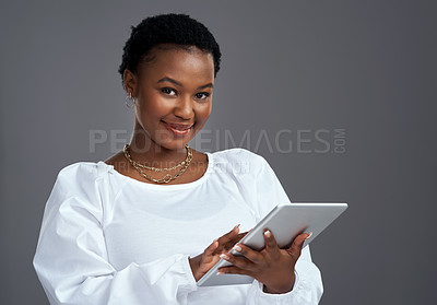 Buy stock photo Shot of a young woman using a digital tablet while standing against a grey background
