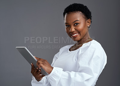Buy stock photo Shot of a young woman using a digital tablet while standing against a grey background