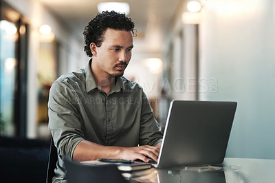 Buy stock photo Shot of a handsome young businessman sitting alone in the office and using his laptop