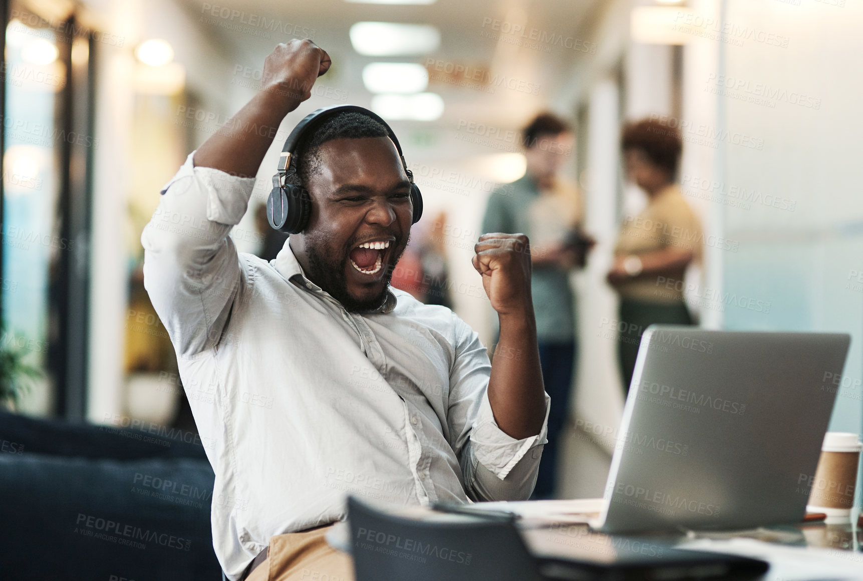 Buy stock photo Shot of a young businessman sitting and celebrating an achievement while wearing headphones and using his laptop