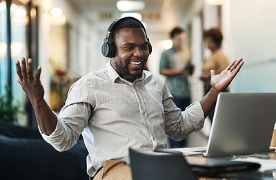 Buy stock photo Shot of a young businessman sitting and celebrating an achievement while wearing headphones and using his laptop