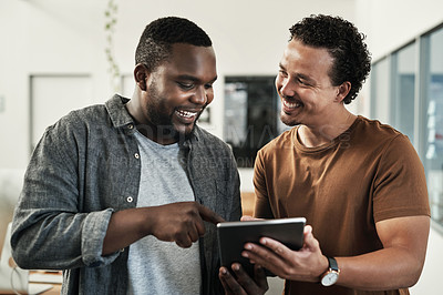 Buy stock photo Shot of two young businessmen standing together and using a digital tablet in the office