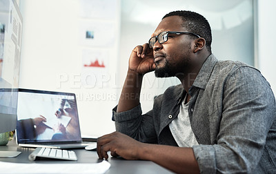 Buy stock photo Shot of a handsome young businessman sitting alone in the office and looking contemplative while using his computer