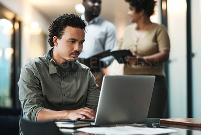 Buy stock photo Shot of a handsome young businessman sitting in the office and using his laptop