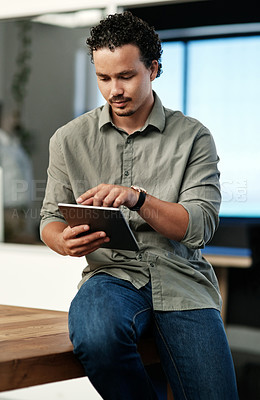 Buy stock photo Shot of a handsome young businessman sitting alone in the office and using a digital tablet