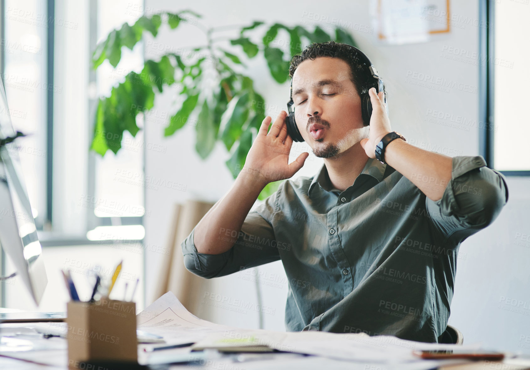 Buy stock photo Shot of a young businessman listening to music in an office