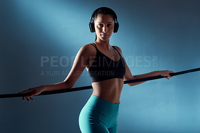 Buy stock photo Studio shot of a sporty young woman wearing headphones and leaning on a rope against a blue background