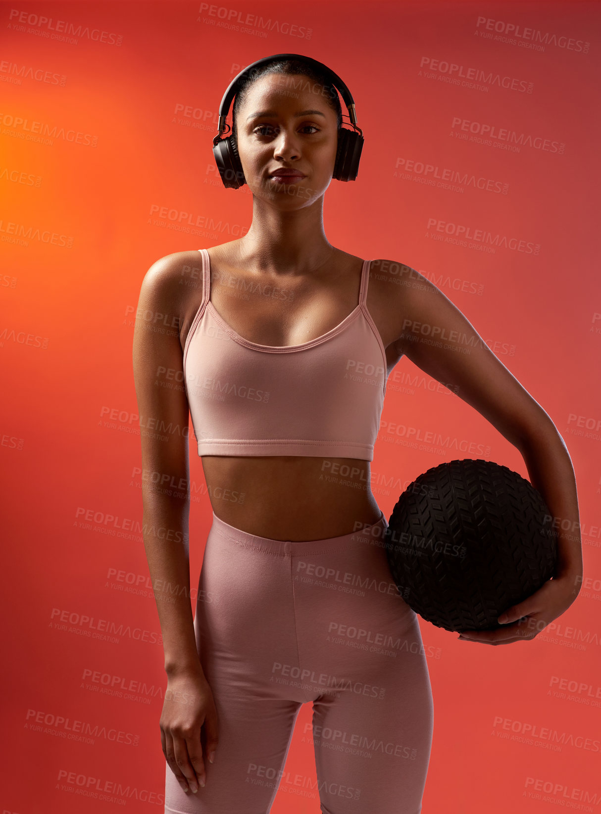 Buy stock photo Studio portrait of a sporty young woman holding an exercise ball against a red background