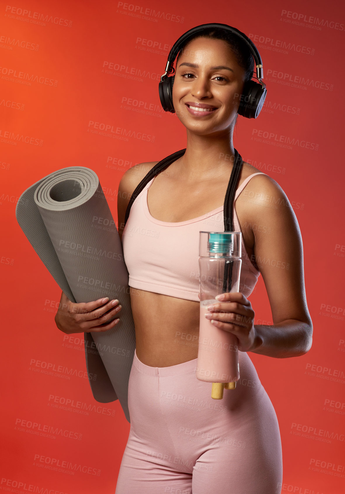 Buy stock photo Studio portrait of a sporty young woman holding a yoga mat and water bottle against a red background