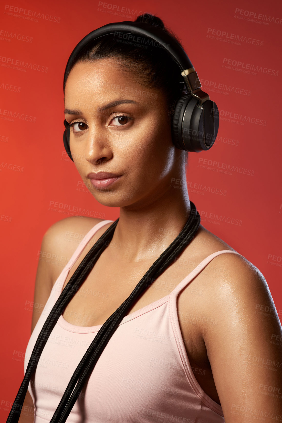 Buy stock photo Studio portrait of a sporty young woman posing with a skipping rope around her neck against a red background