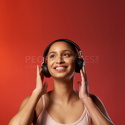 Buy stock photo Studio shot of a sporty young woman listening to music against a red background