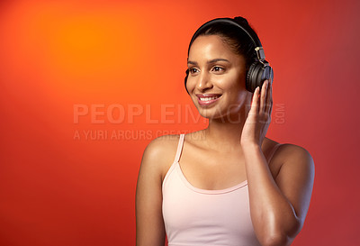 Buy stock photo Studio shot of a sporty young woman listening to music against a red background