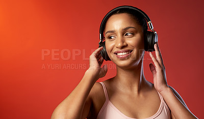 Buy stock photo Studio shot of a sporty young woman listening to music against a red background