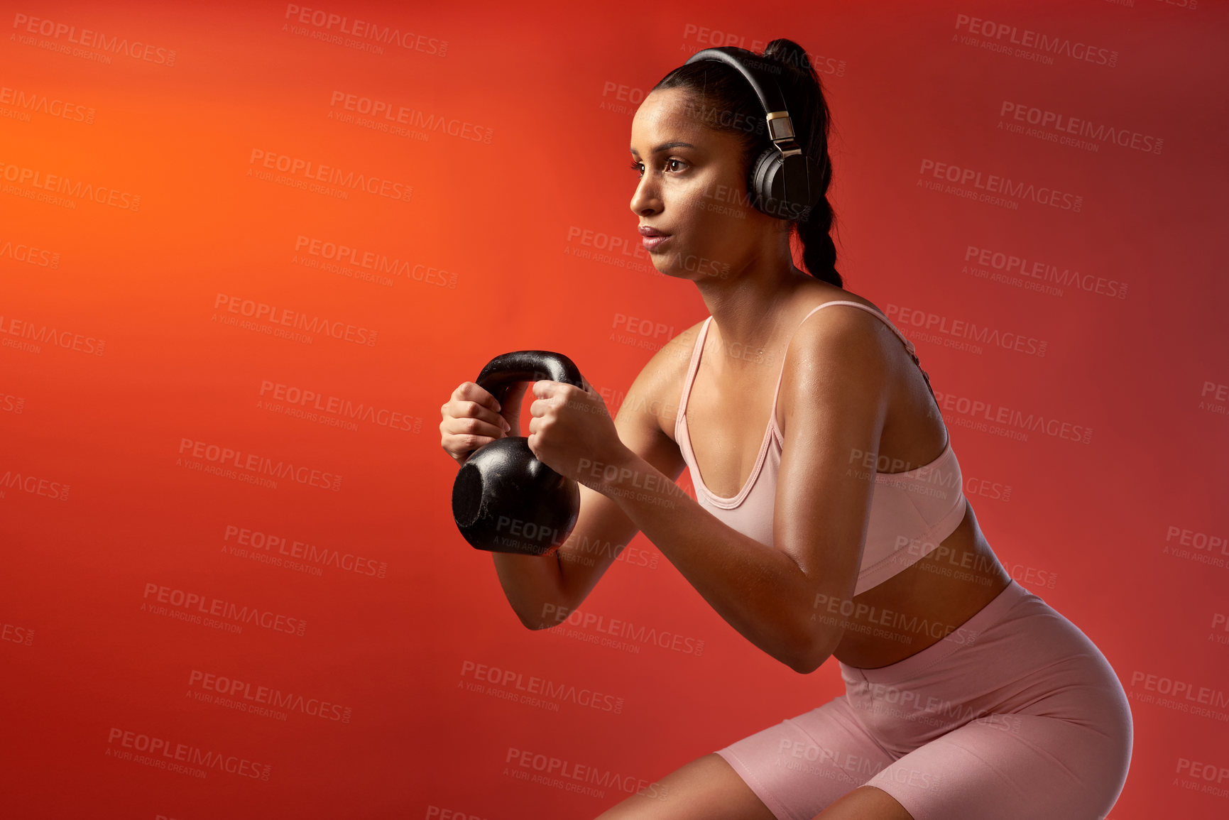 Buy stock photo Studio shot of a sporty young woman doing kettlebell squats against a red background