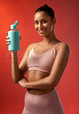 Buy stock photo Studio portrait of a sporty young woman holding a water bottle against a red background