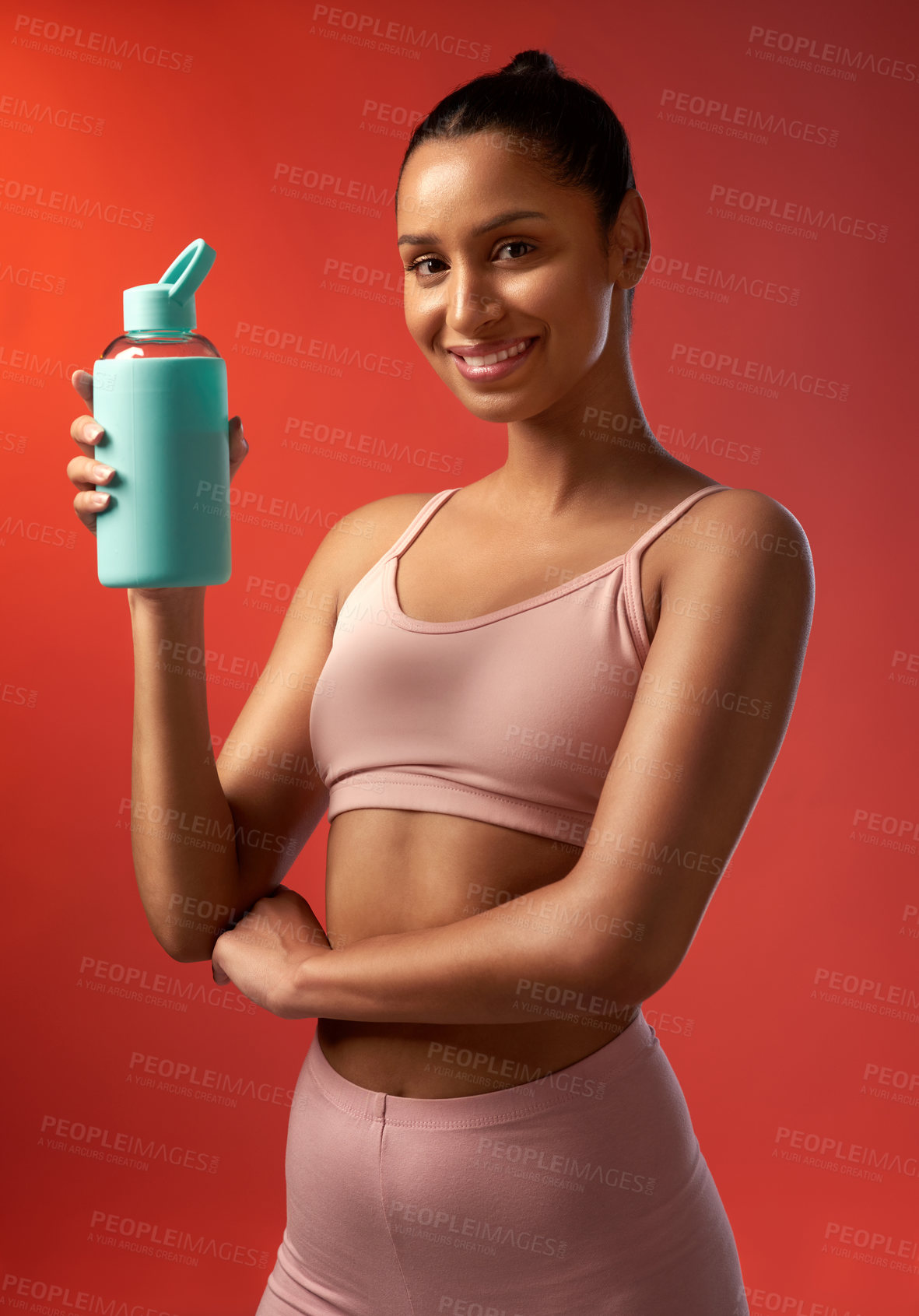 Buy stock photo Studio portrait of a sporty young woman holding a water bottle against a red background