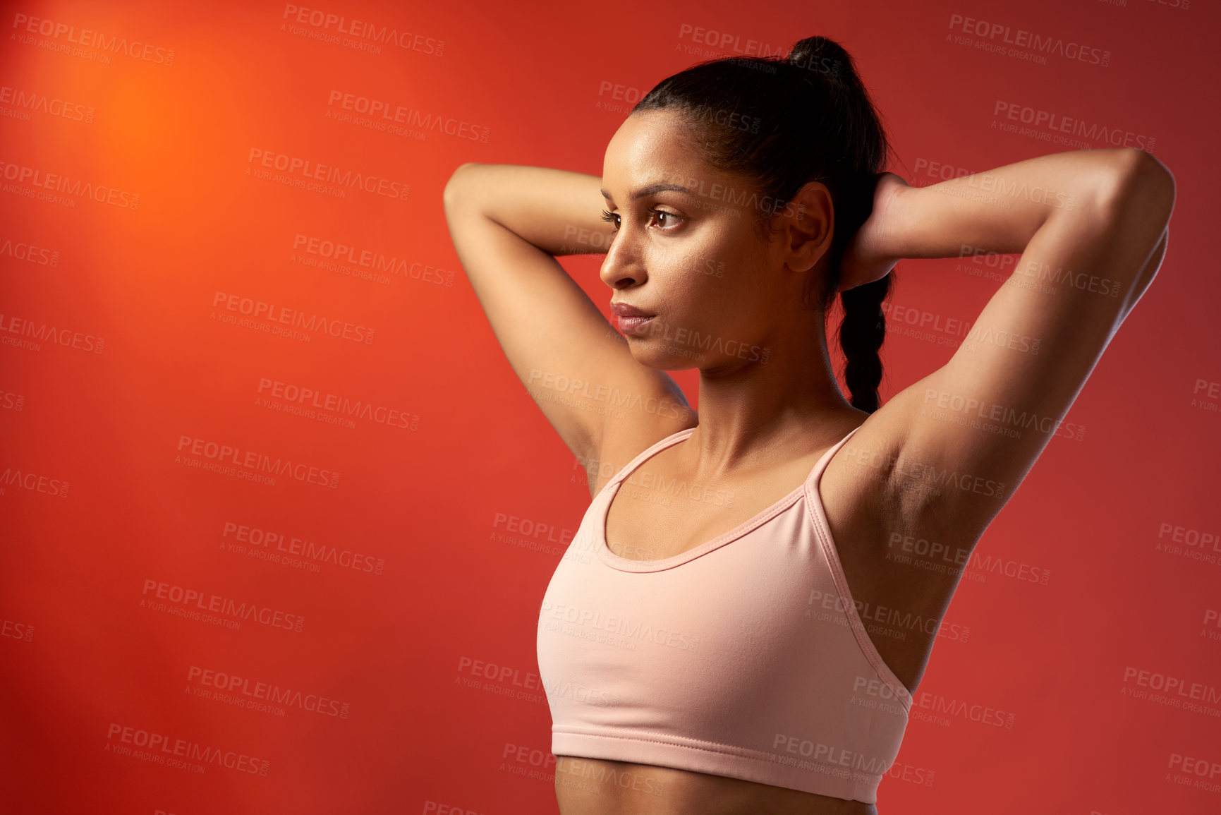 Buy stock photo Studio shot of a sporty young woman stretching her arms against a red background