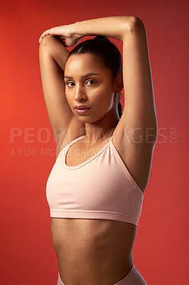 Buy stock photo Studio portrait of a sporty young woman stretching her arms against a red background