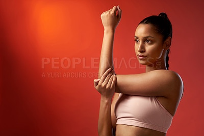 Buy stock photo Studio shot of a sporty young woman stretching her arms against a red background
