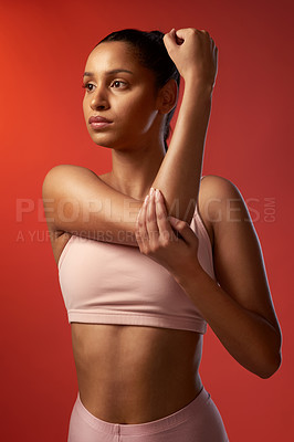 Buy stock photo Studio shot of a sporty young woman stretching her arms against a red background