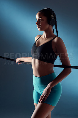 Buy stock photo Studio shot of a sporty young woman wearing headphones and leaning on a rope against a blue background