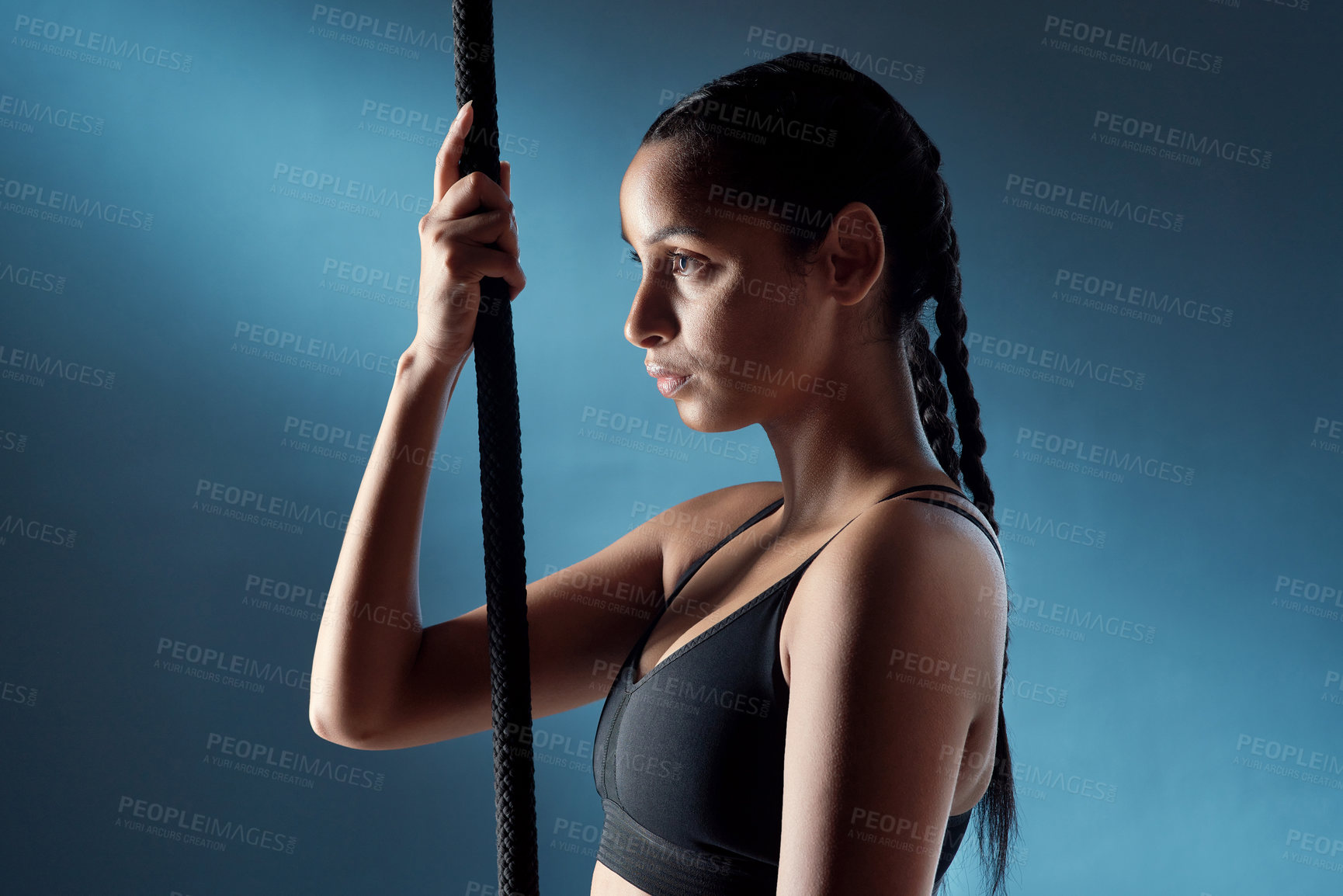 Buy stock photo Studio shot of a sporty young woman getting ready to climb a rope against a blue background