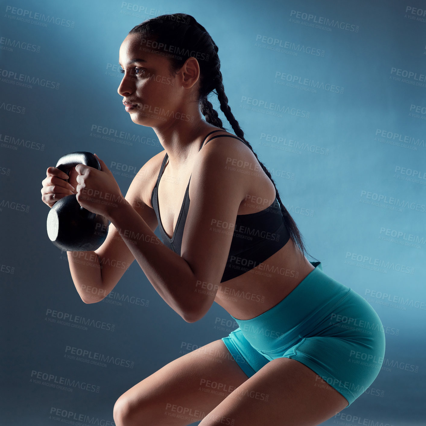 Buy stock photo Studio shot of a sporty young woman doing kettlebell squats against a blue background