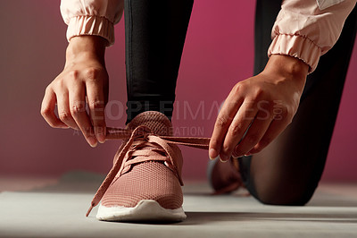 Buy stock photo Studio shot of an unrecognisable woman tying her shoelaces against a red background