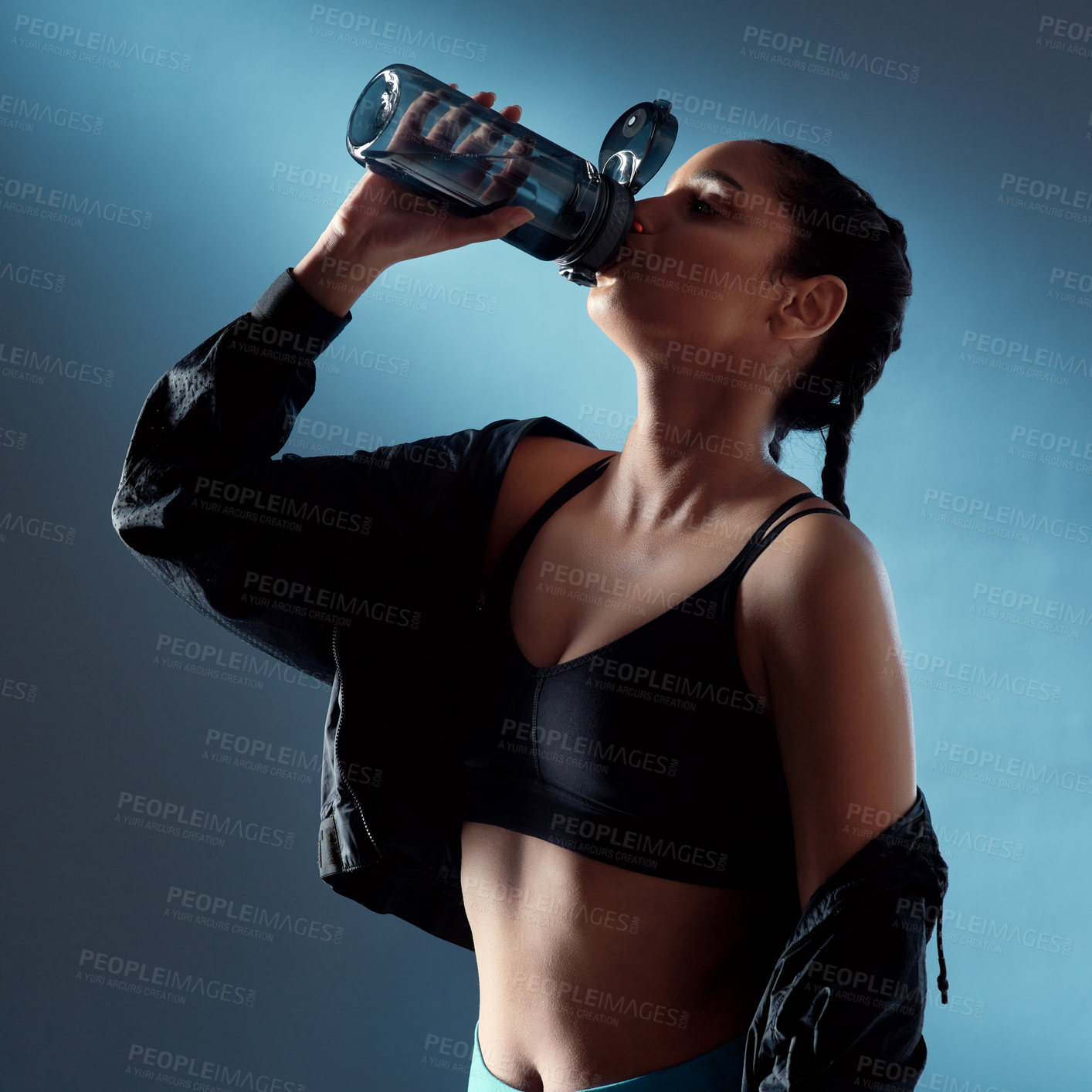 Buy stock photo Studio shot of a sporty young woman drinking water against a blue background