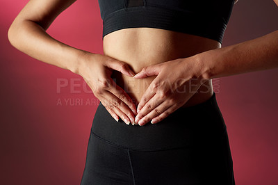 Buy stock photo Studio shot of an unrecognisable woman making a heart shape with her hands on her stomach against a red background