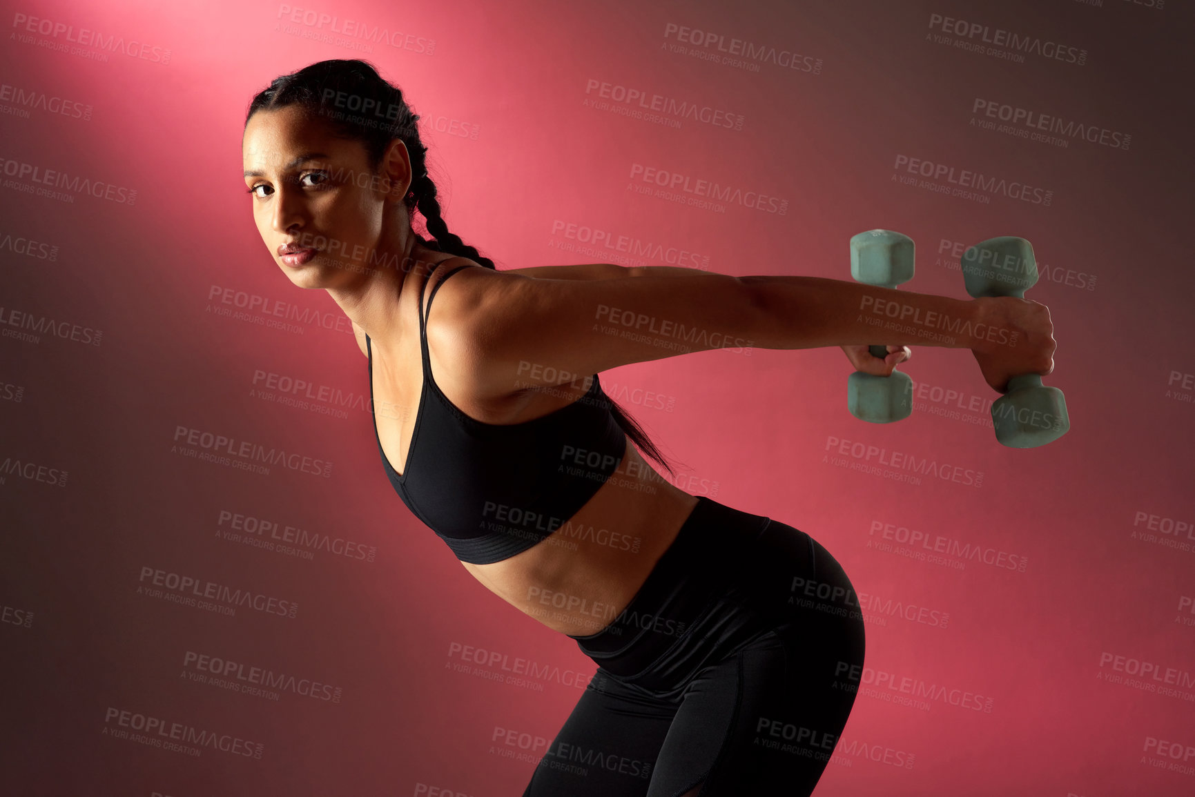 Buy stock photo Studio portrait of a sporty young woman exercising with dumbbells against a red background