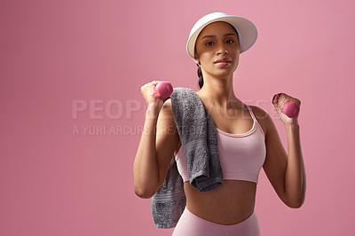 Buy stock photo Cropped portrait of an attractive and sporty young woman posing with a towel and dumbbells in studio against a pink background