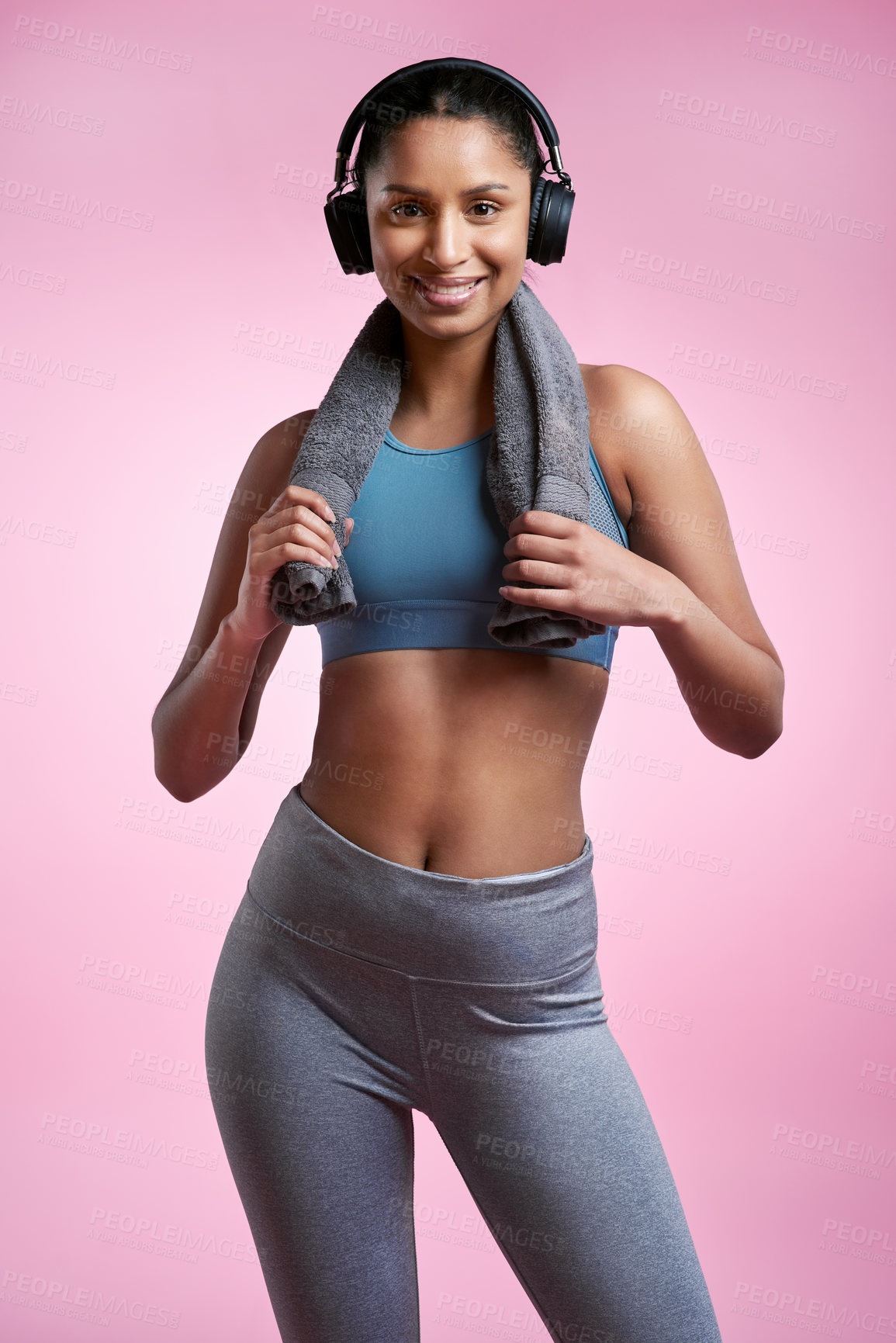 Buy stock photo Cropped portrait of an attractive and sporty young woman wearing headphones and posing with a towel in studio against a pink background