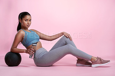 Buy stock photo Full length portrait of an attractive and sporty young woman posing with a medicine ball and water bottle in studio against a pink background