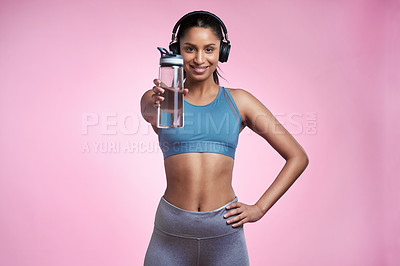 Buy stock photo Cropped portrait of an attractive and sporty young woman wearing headphones and posing with a water bottle in studio against a pink background