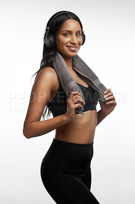 Buy stock photo Studio portrait of a sporty young woman wearing headphones and holding a towel around her neck against a white background