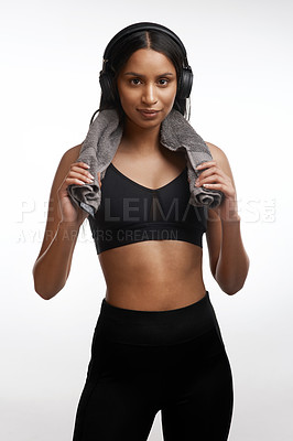 Buy stock photo Studio portrait of a sporty young woman wearing headphones and holding a towel around her neck against a white background