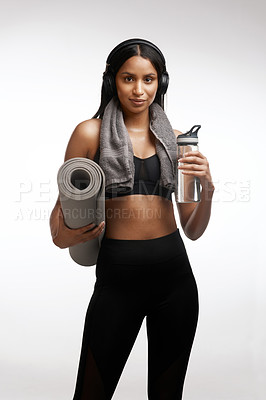 Buy stock photo Studio portrait of a sporty young woman holding a yoga mat and water bottle against a white background