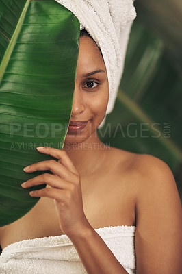 Buy stock photo Shot of a beautiful young woman wearing a towel around her head while posing behind a green leaf