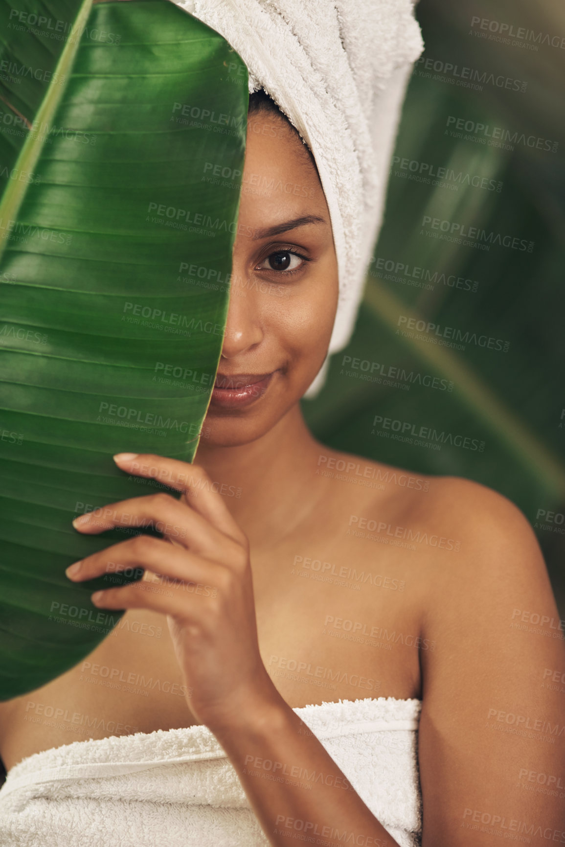 Buy stock photo Shot of a beautiful young woman wearing a towel around her head while posing behind a green leaf