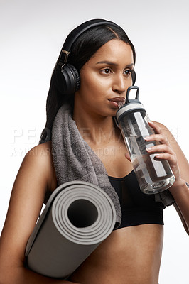 Buy stock photo Studio shot of a sporty young woman drinking water and holding a yoga mat against a white background