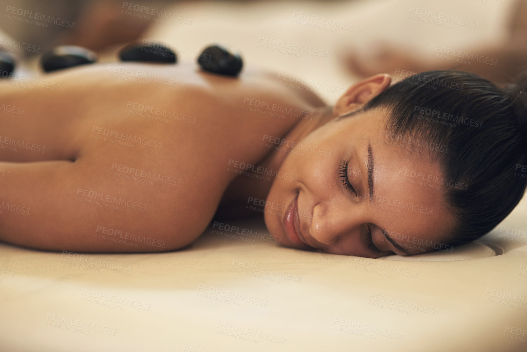 Buy stock photo Shot of a young woman enjoying a hot stone massage at a spa