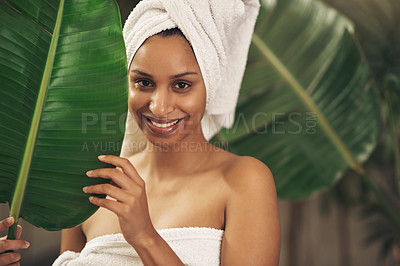 Buy stock photo Shot of a beautiful young woman wearing a towel around her head while posing behind a green leaf