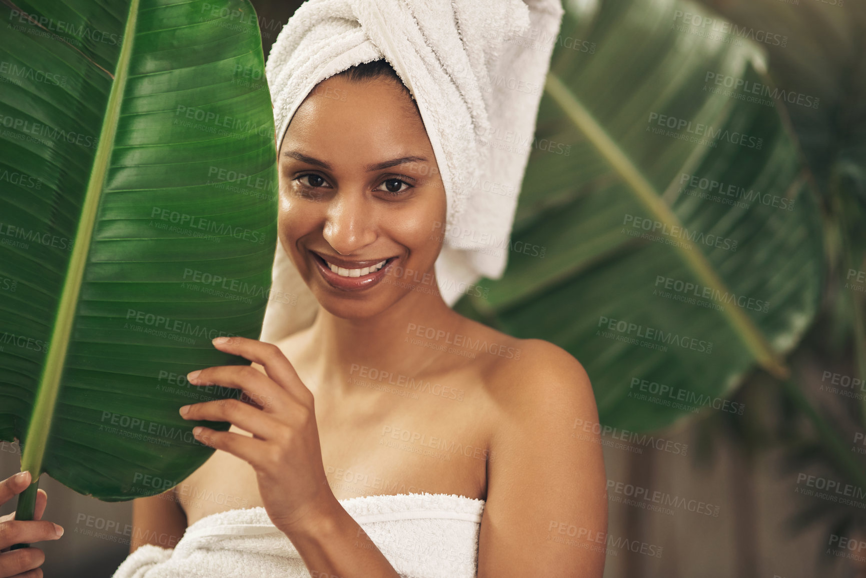 Buy stock photo Shot of a beautiful young woman wearing a towel around her head while posing behind a green leaf