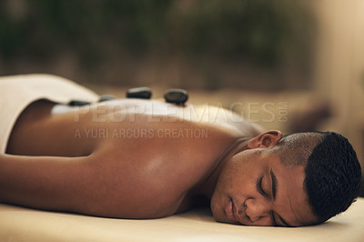 Buy stock photo Shot of a young man getting a hot stone massage at a spa