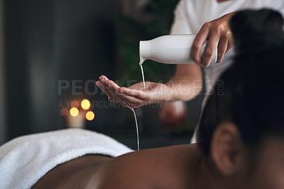 Buy stock photo Closeup shot of a massage therapist pouring body oil into her hands while giving a massage to a customer at a spa