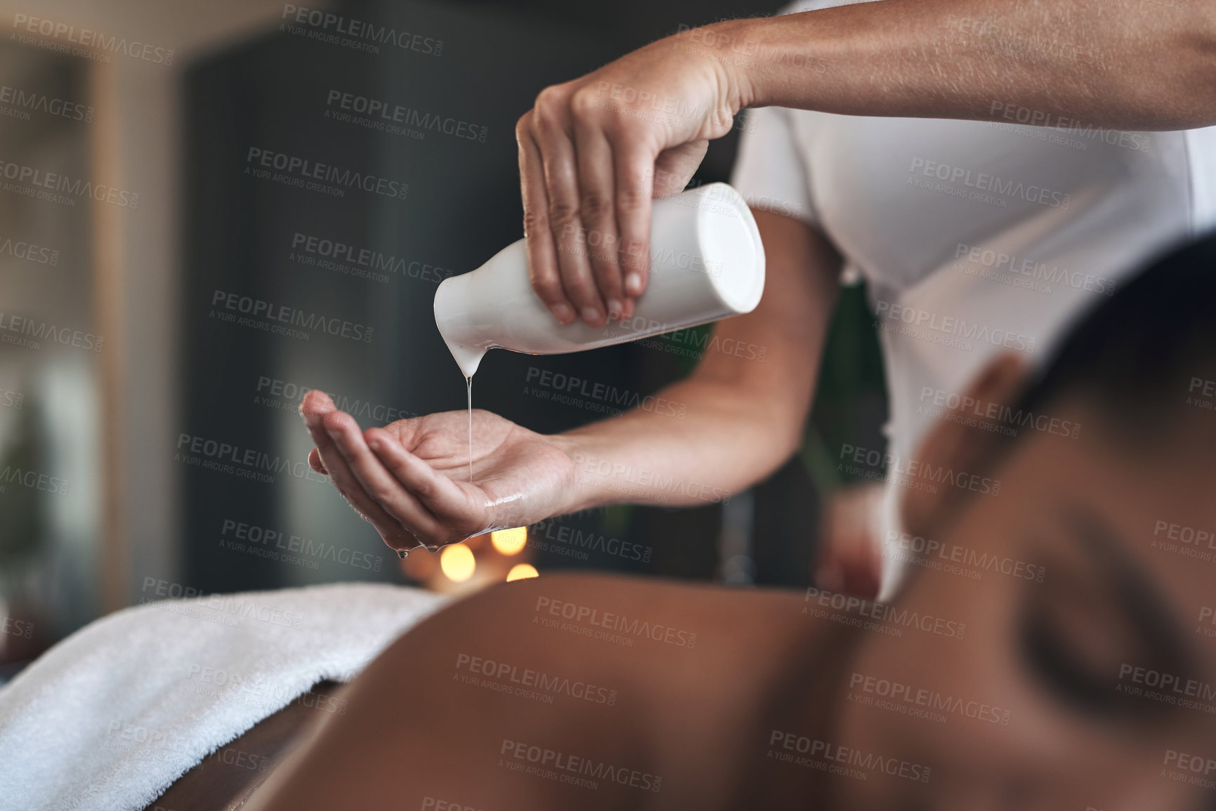 Buy stock photo Closeup shot of a massage therapist pouring body oil into her hands while giving a massage to a customer at a spa