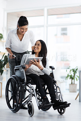 Buy stock photo Full length shot of an attractive young businesswoman in a wheelchair talking to the female colleague pushing her through the office